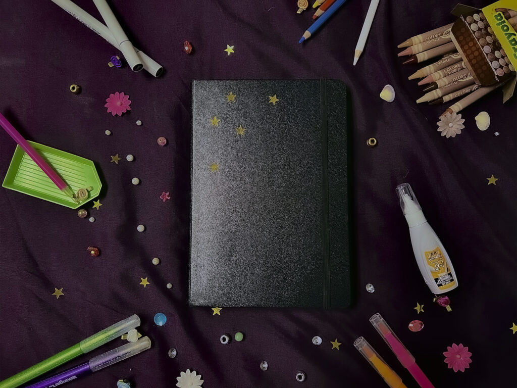 a book surrounded by other stationary like pens and sequins